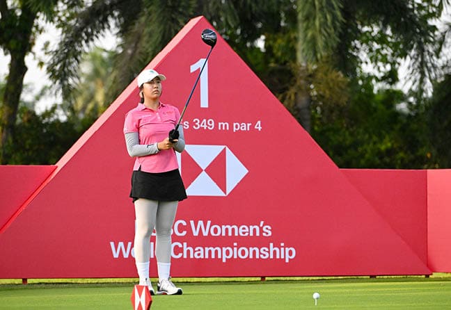 A woman in a pink shirt and black shorts is holding a golf club and standing on a golf course. AI generated content