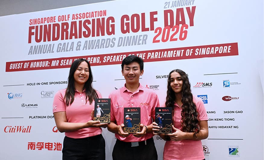 Three people are holding up trophies, with two of them wearing pink shirts. They are standing in front of a sign that says “Singapore Golf Association Golf Day 2026 Fundraising Gala & Awards Dinner." AI generated content